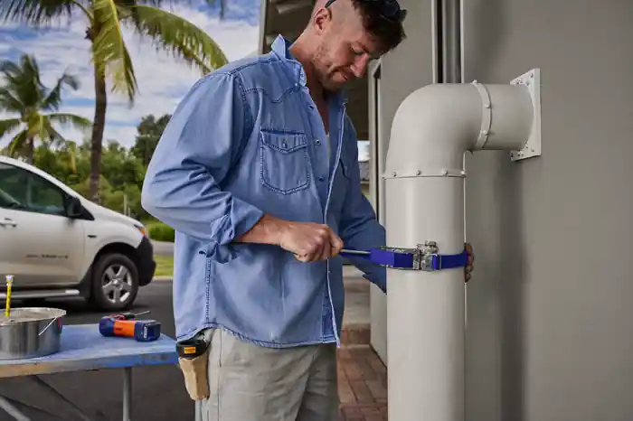 Radon mitigation technician strapping a PVC vent pipe to the exterior wall of a Jacksonville home